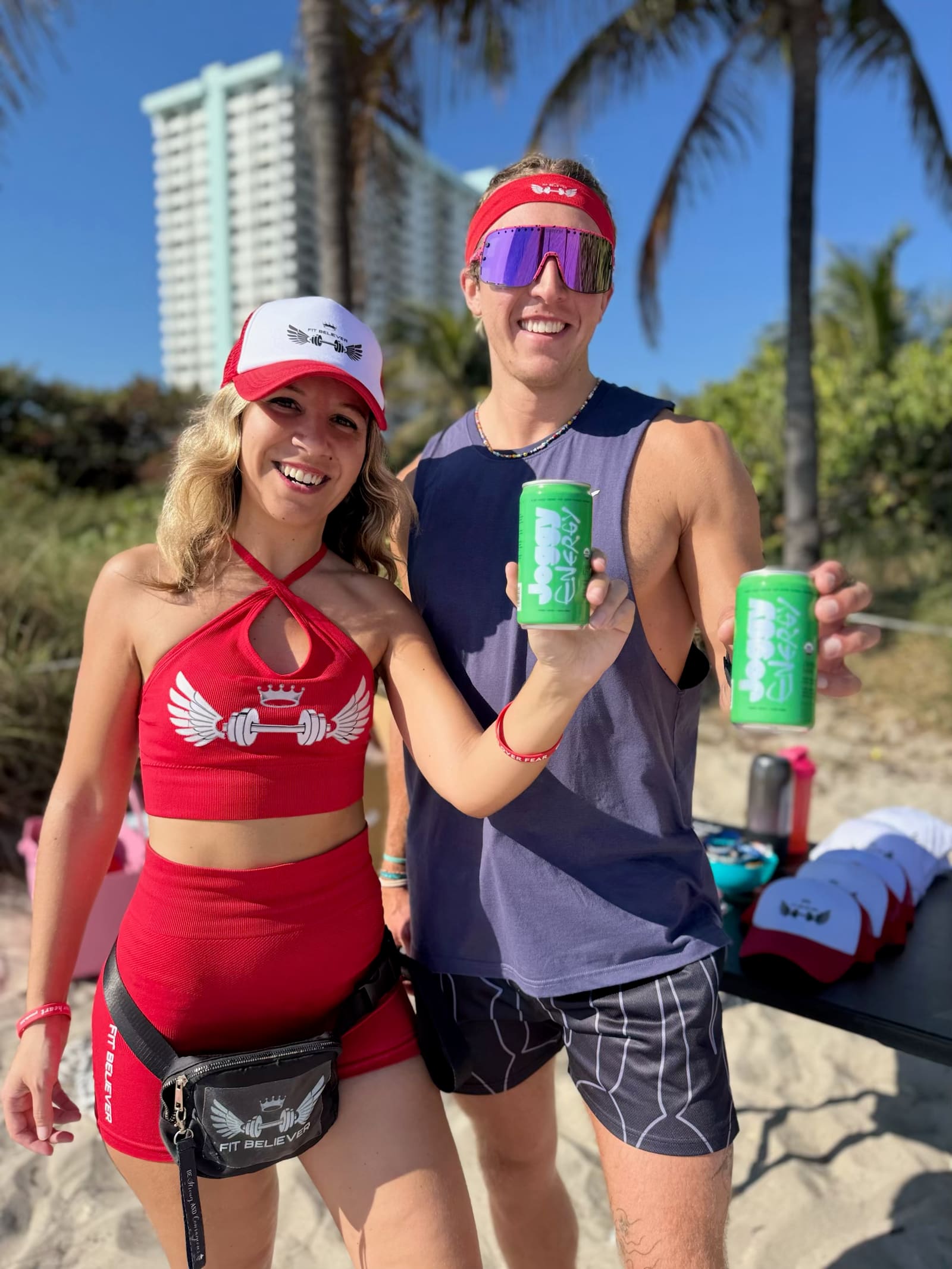 Two people on the beach smiling and holding up cans of Joggy Energy