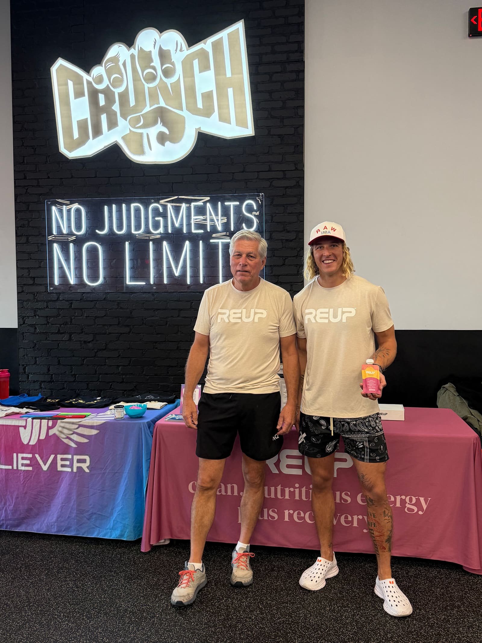 Max and a teammate in Reup shirts in front of a Reup table inside a Crunch Fitness gym
