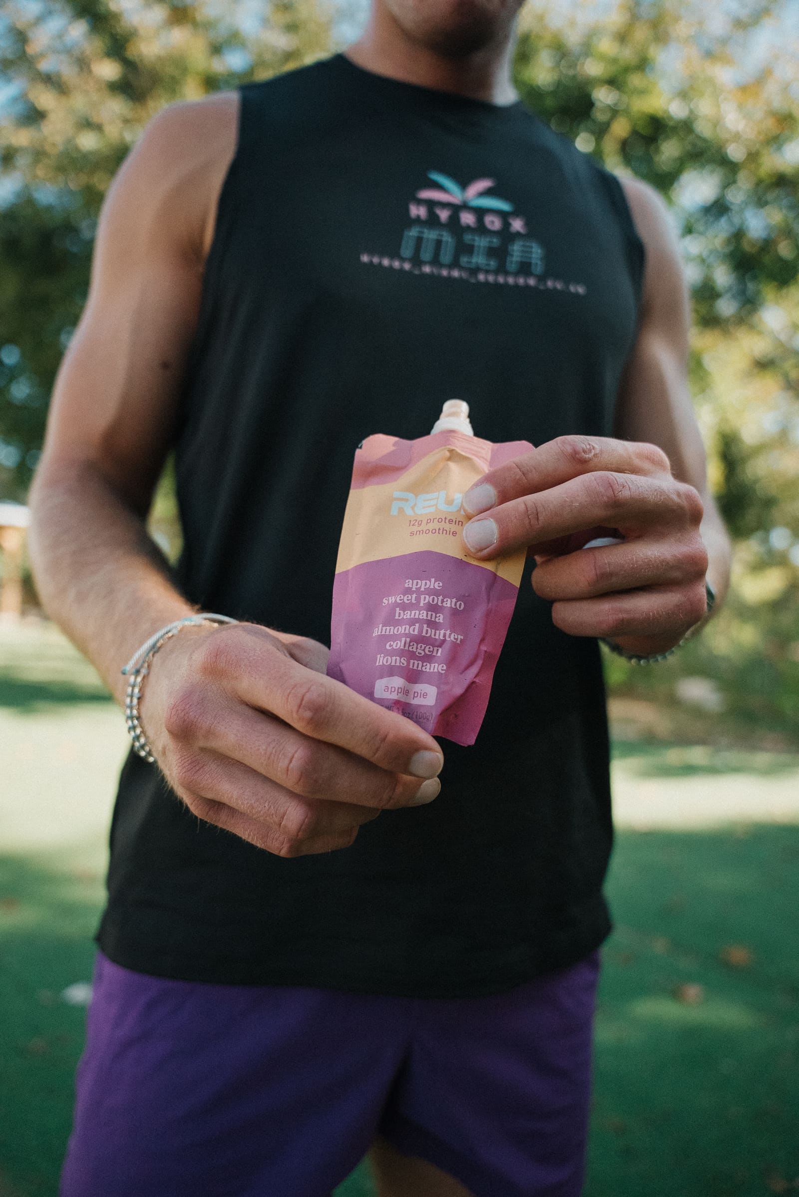 An athlete in a HYROX Miami tank holding a Reup protein smoothie pouch